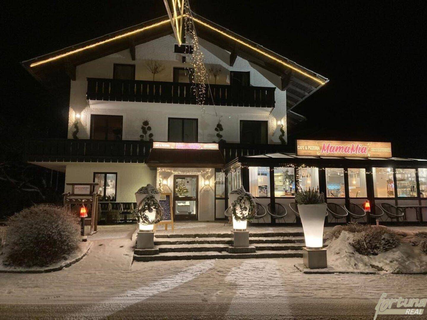 Winterliche Ansicht des Gebäudes bei Nacht, festlich beleuchtet mit Schnee und Weihnachtsdekoration.