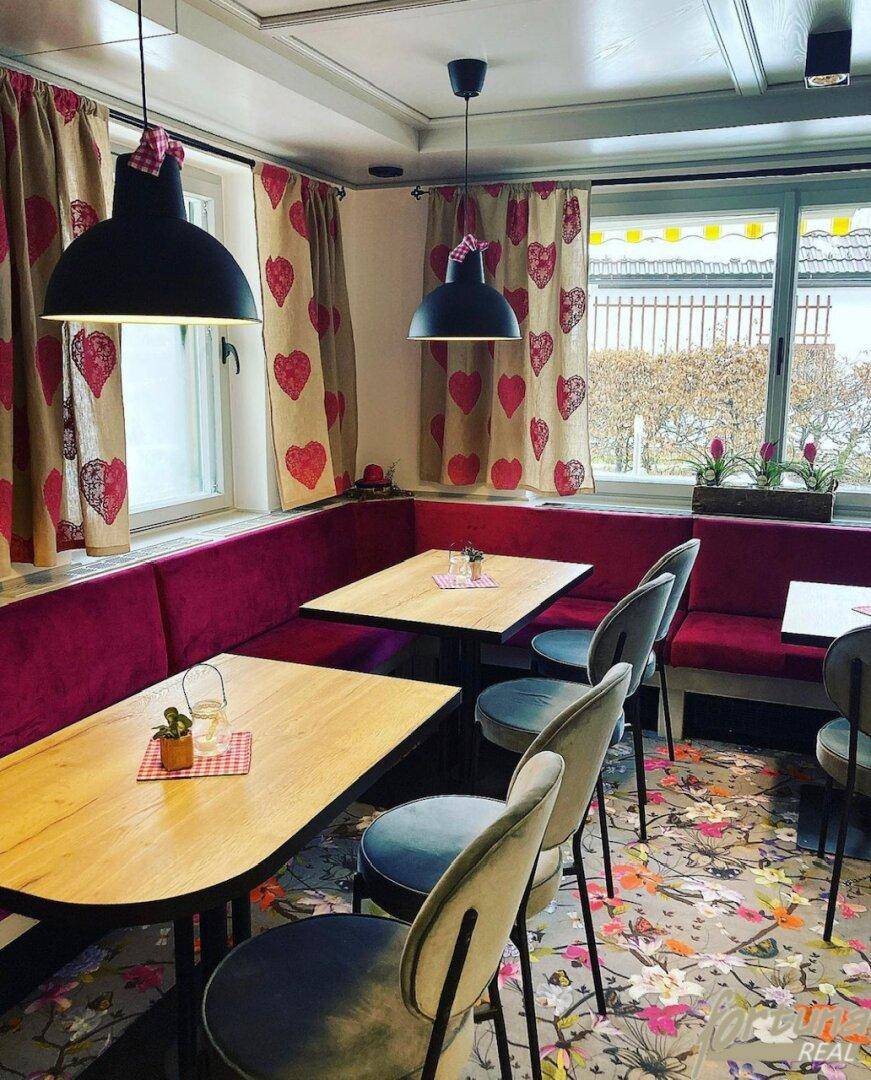 Traditioneller Essbereich mit roten Sitzbänken, Holztischen und floralem Teppichboden.