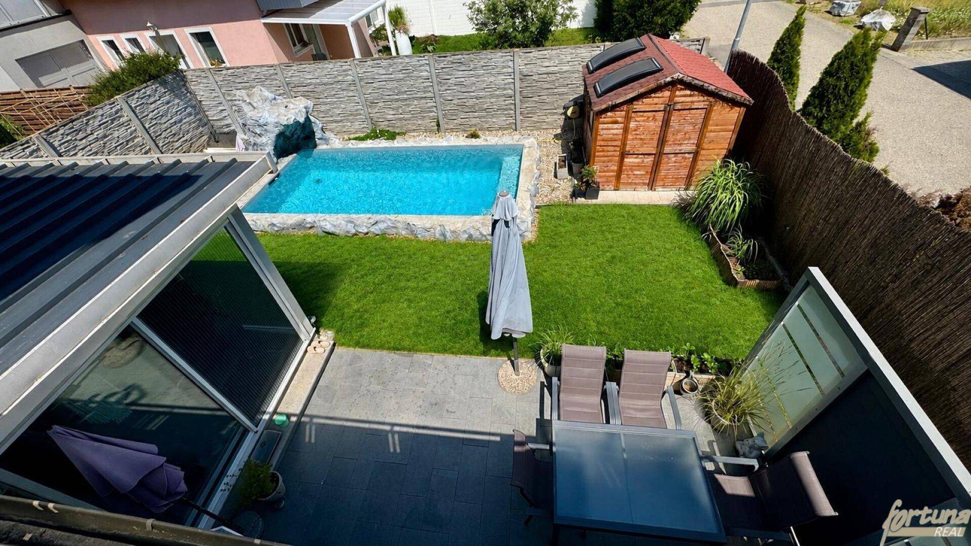 Vogelperspektive des Gartens mit Pool, Gartenhaus und möblierter Terrasse.