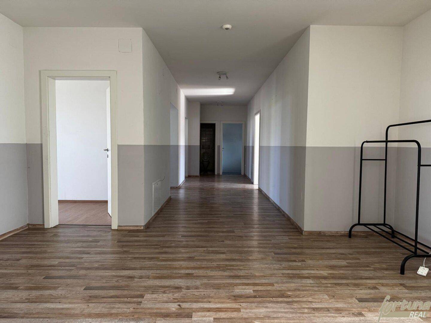 Langer Flur mit Laminatboden und zweifarbigen Wänden, der zu weiteren Räumen führt.