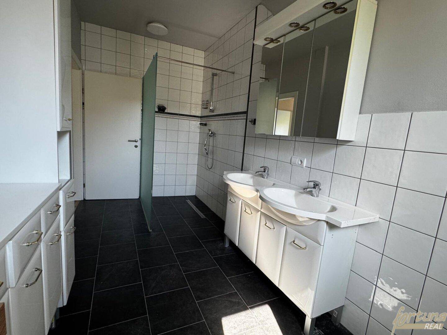 Badezimmer mit Doppelwaschbecken, Spiegelschrank und Duschbereich mit Glaswand.