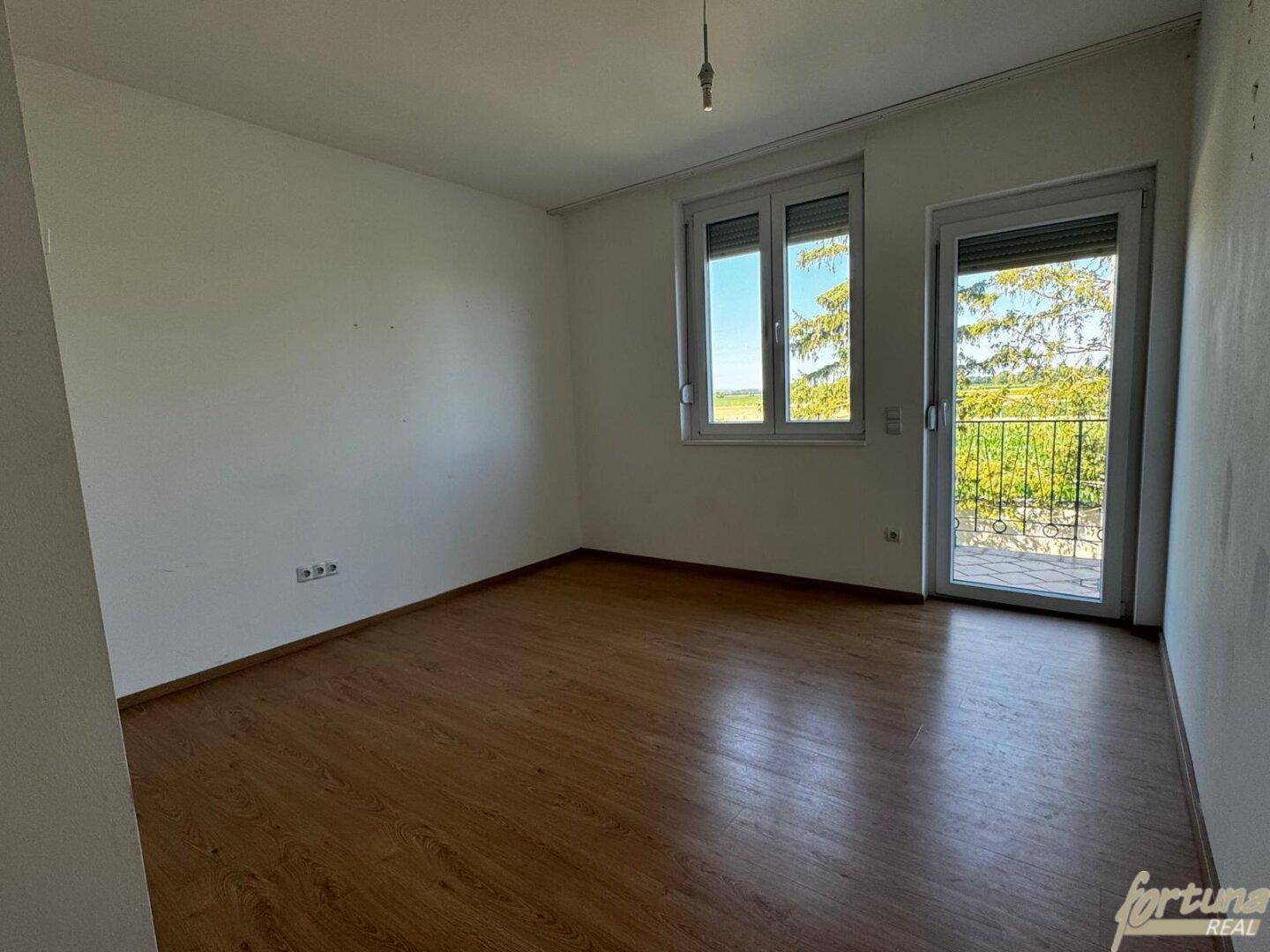 Helles Schlafzimmer mit Laminatboden und Zugang zu einem französischen Balkon.