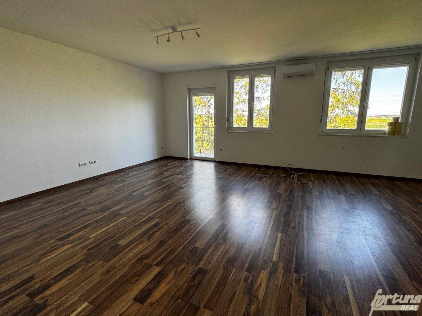 Geräumiges Wohnzimmer mit dunklem Laminatboden und Zugang zu einem Balkon.