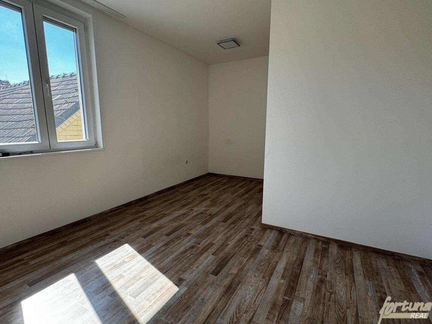 Helles Schlafzimmer mit Laminatboden und einem Fenster, das viel Tageslicht hereinlässt.