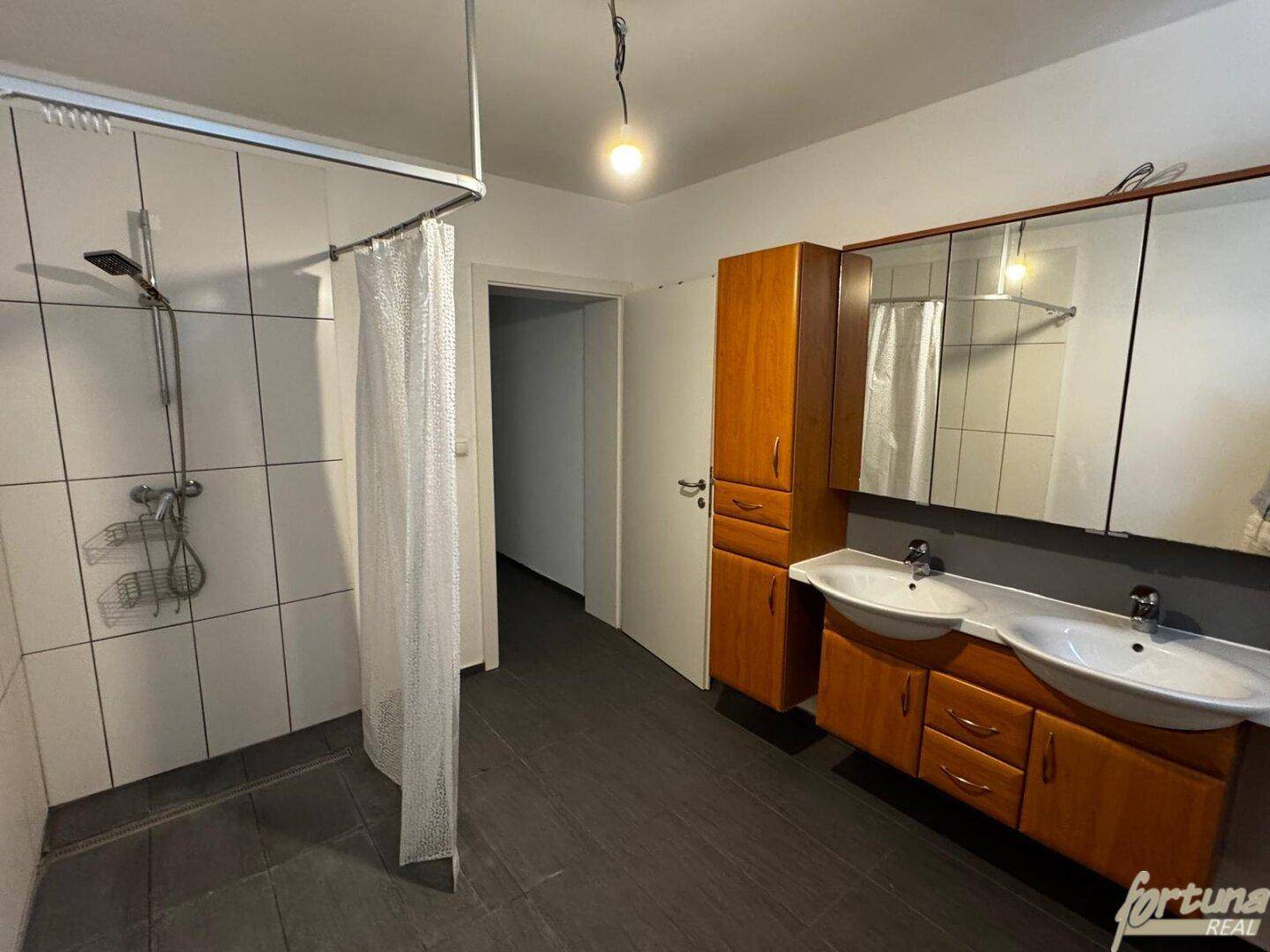 Badezimmer mit Doppelwaschbecken, Spiegelschrank und Duschbereich mit Vorhang.