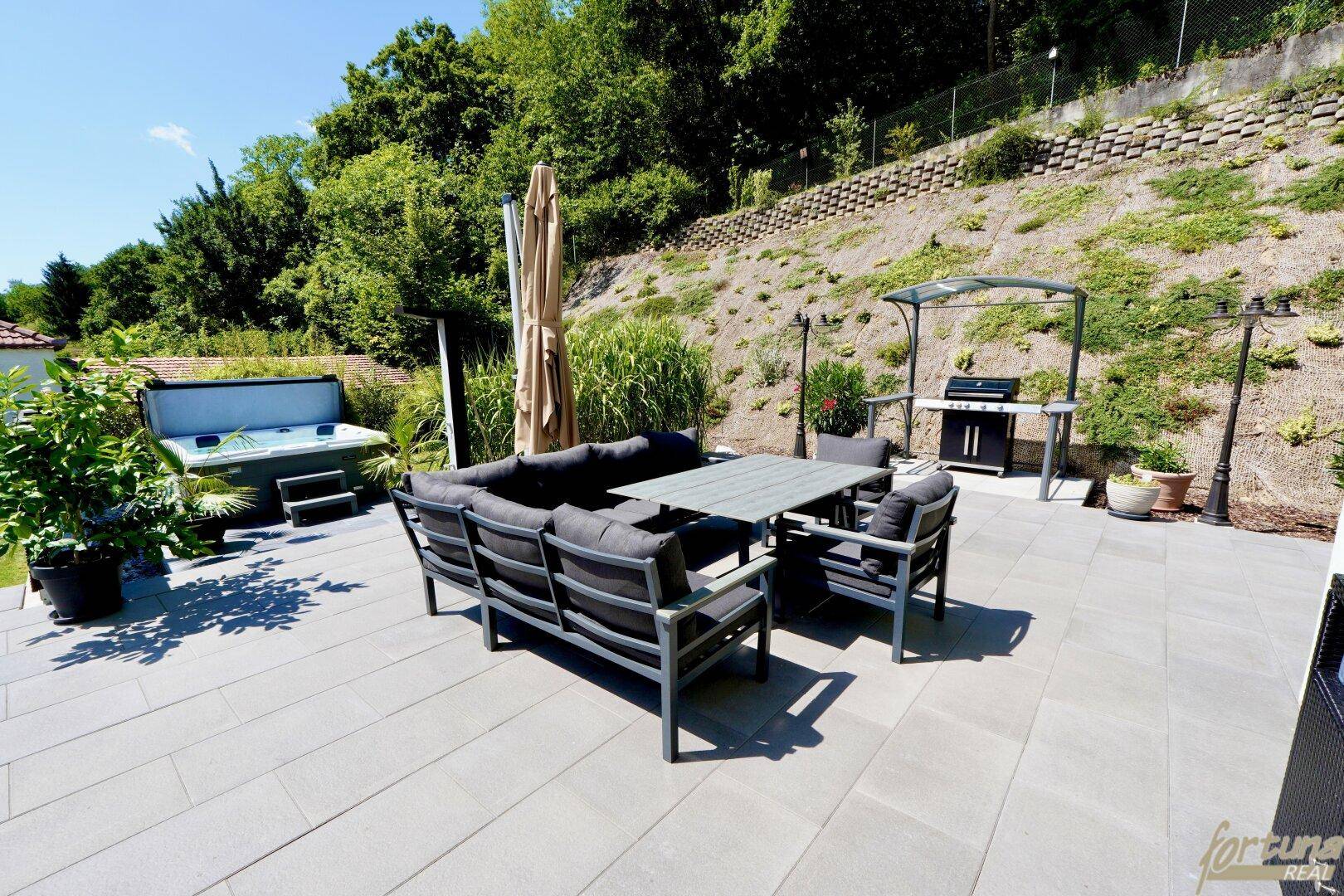 Geräumige Terrasse mit Lounge-Möbeln, Grillbereich und Whirlpool im Hintergrund.