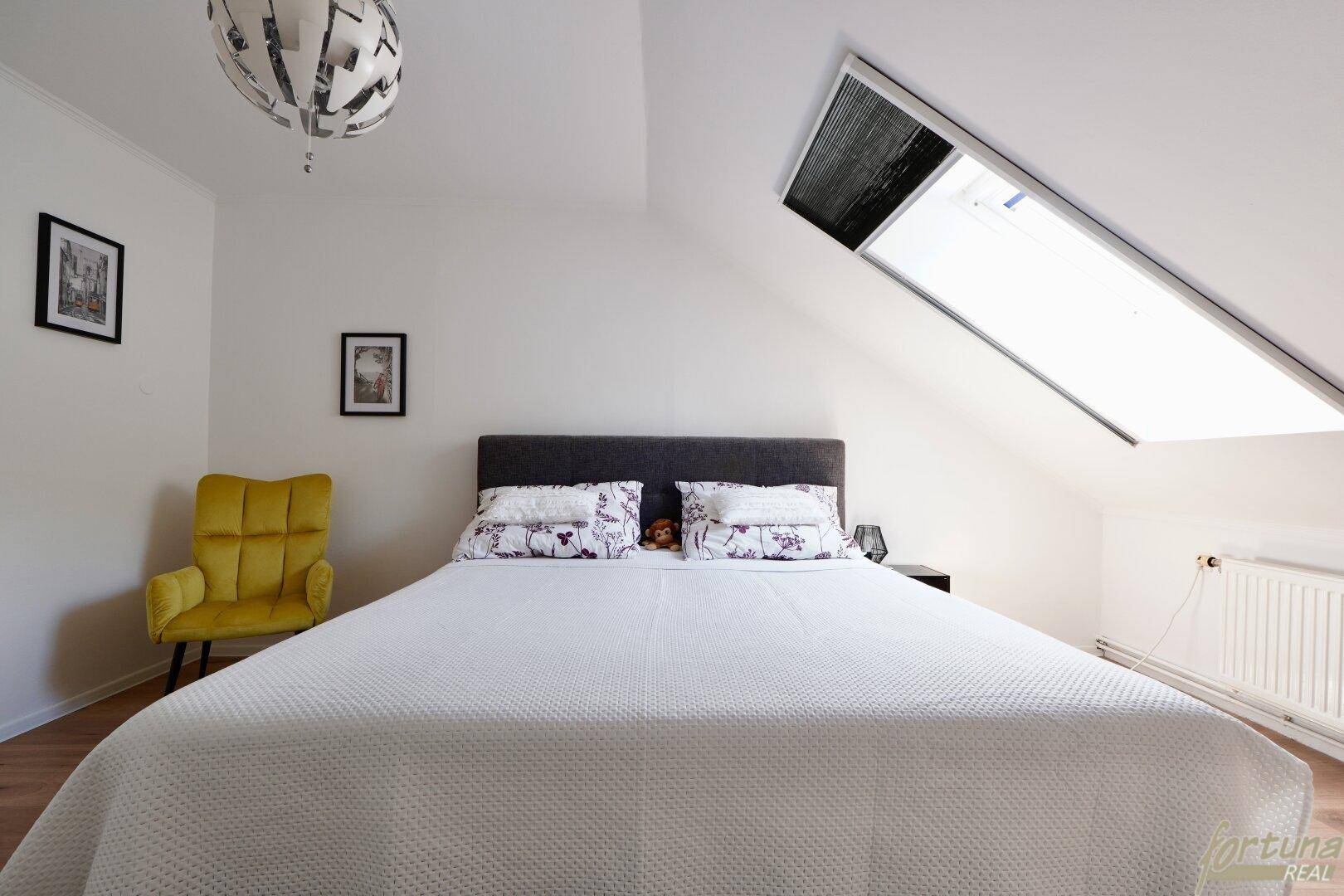 Helles Schlafzimmer im Dachgeschoss mit Dachfenster und Holzboden.