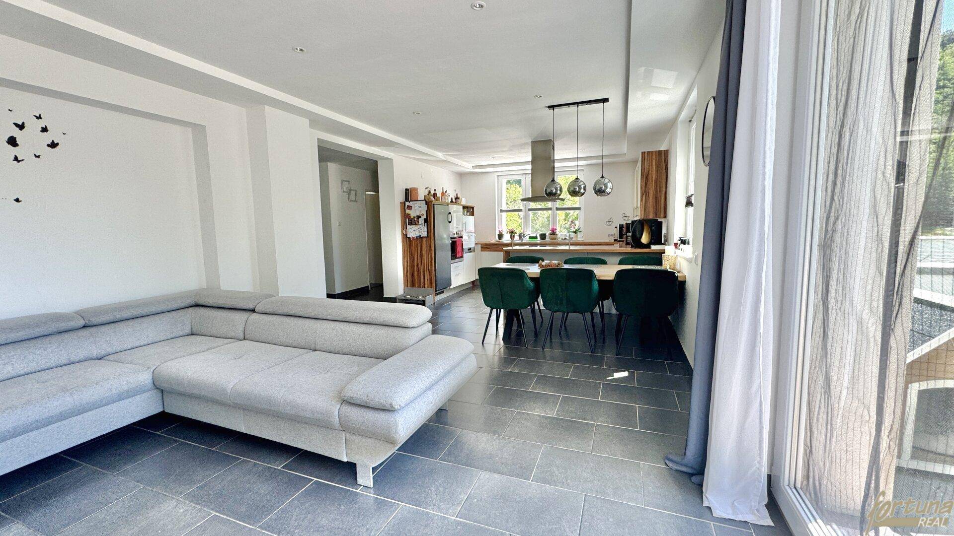 Geräumiger offener Wohnbereich mit großer Couch und Blick auf die Küche.