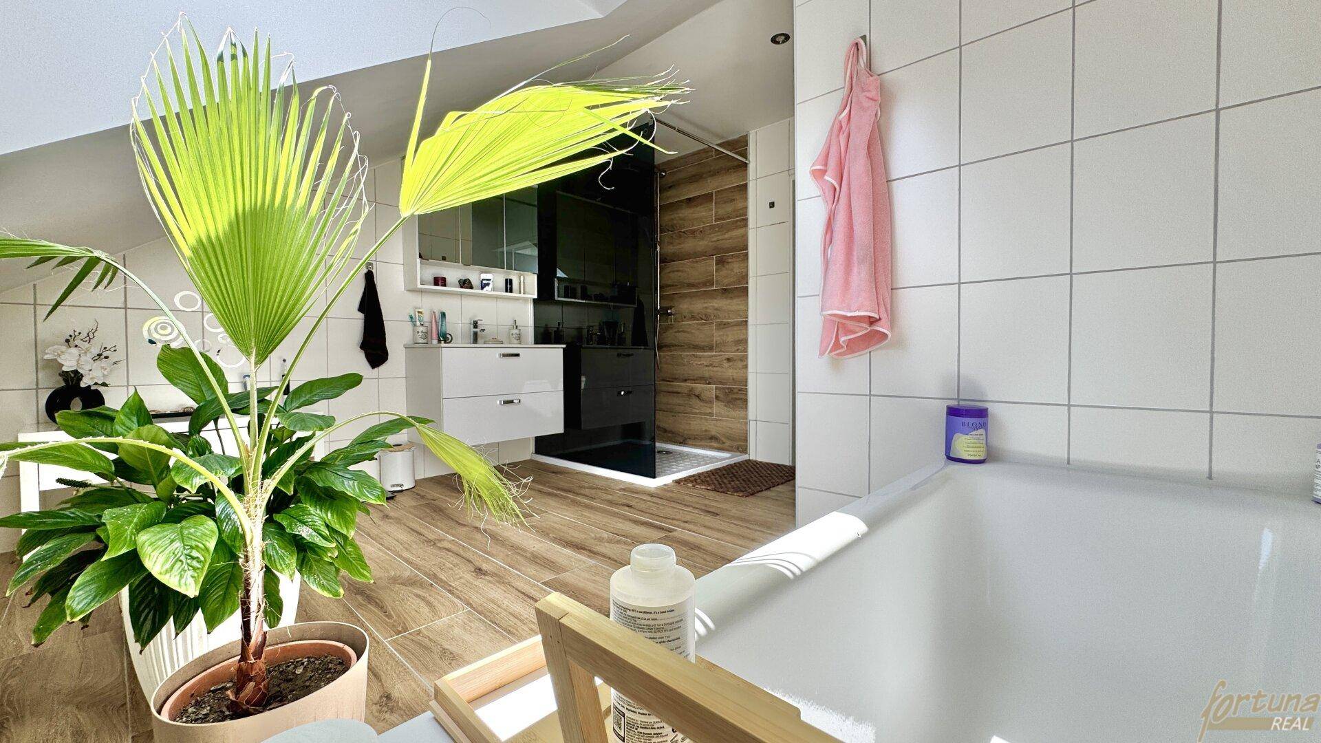 Helles Badezimmer mit Badewanne, begehbarer Dusche und Holzoptik-Fliesen.