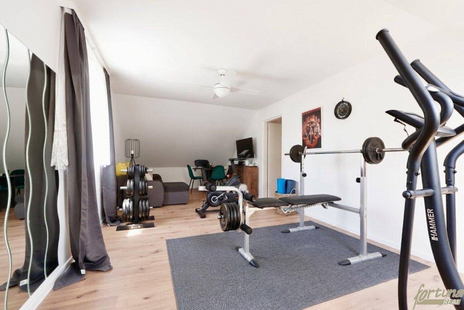 Geräumiger Fitnessraum mit verschiedenen Trainingsgeräten und Holzboden.