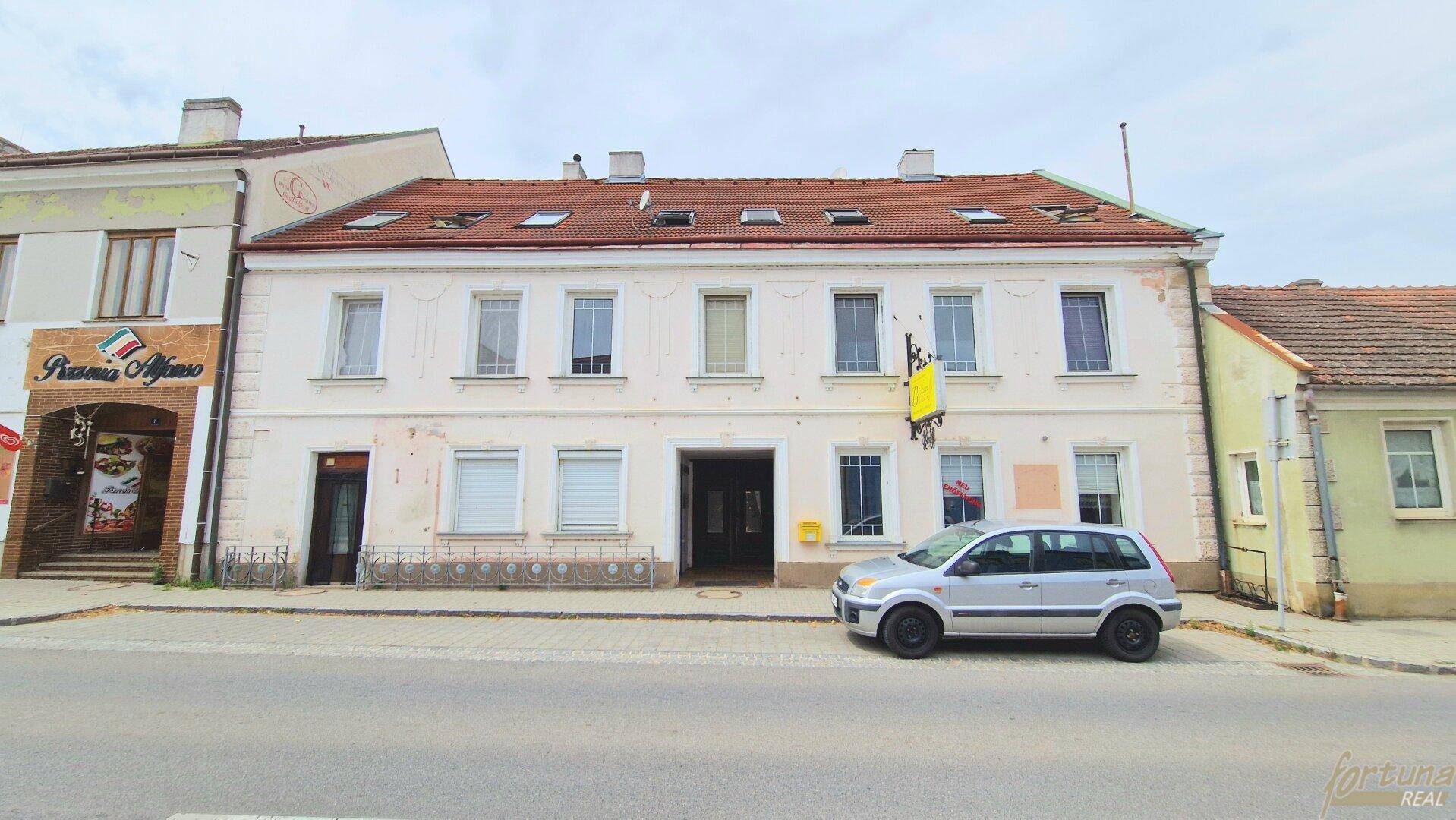 Straßenansicht eines älteren Gebäudes mit mehreren Fenstern und einem geparkten Auto davor.