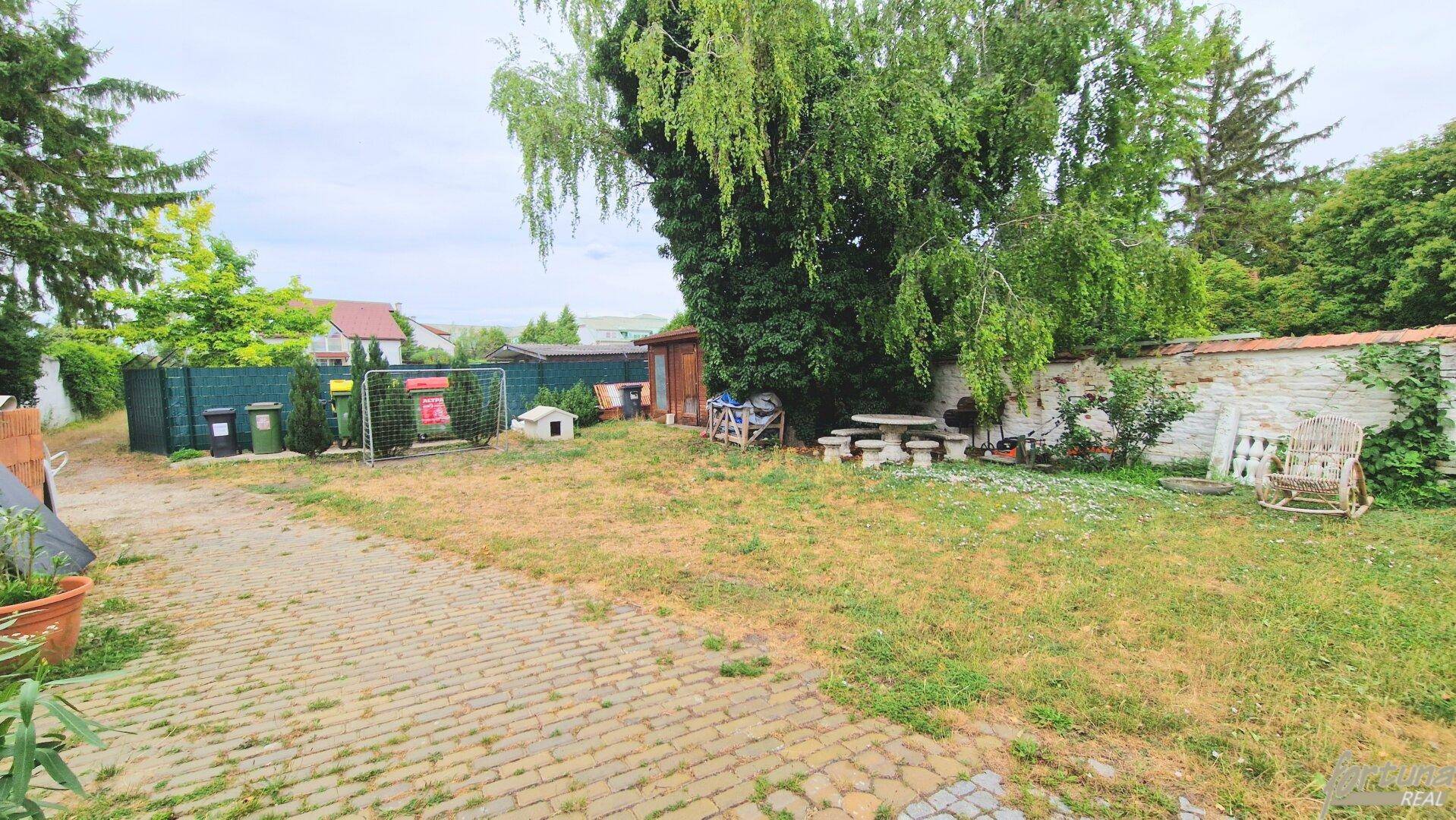 Großer Gartenbereich mit altem Baumbestand, Rasenfläche und einer Steinsitzgruppe im Freien.