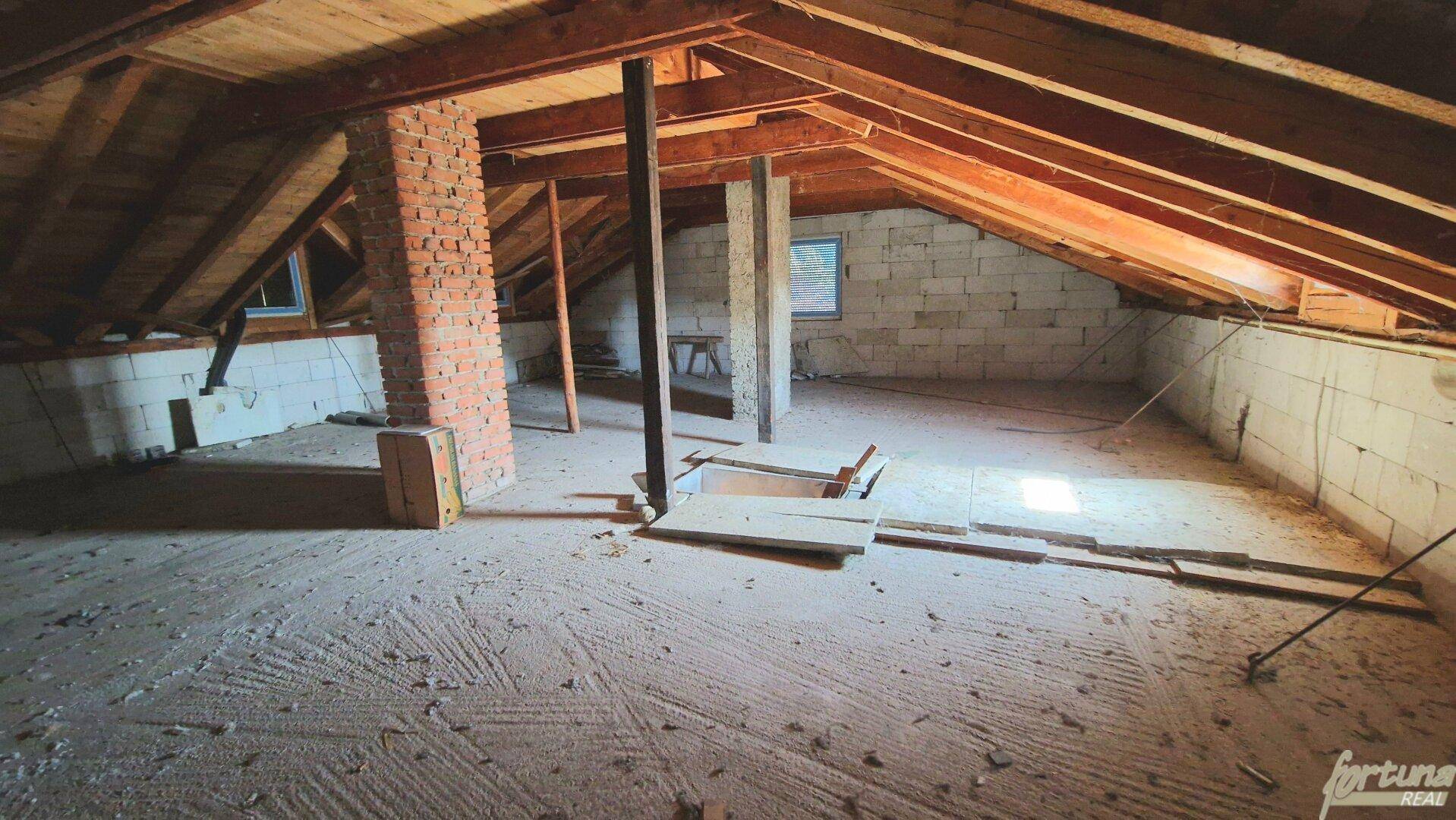 Unausgebauter Dachboden mit sichtbaren Holzbalken und Ziegelkamin, bereit für den Ausbau.