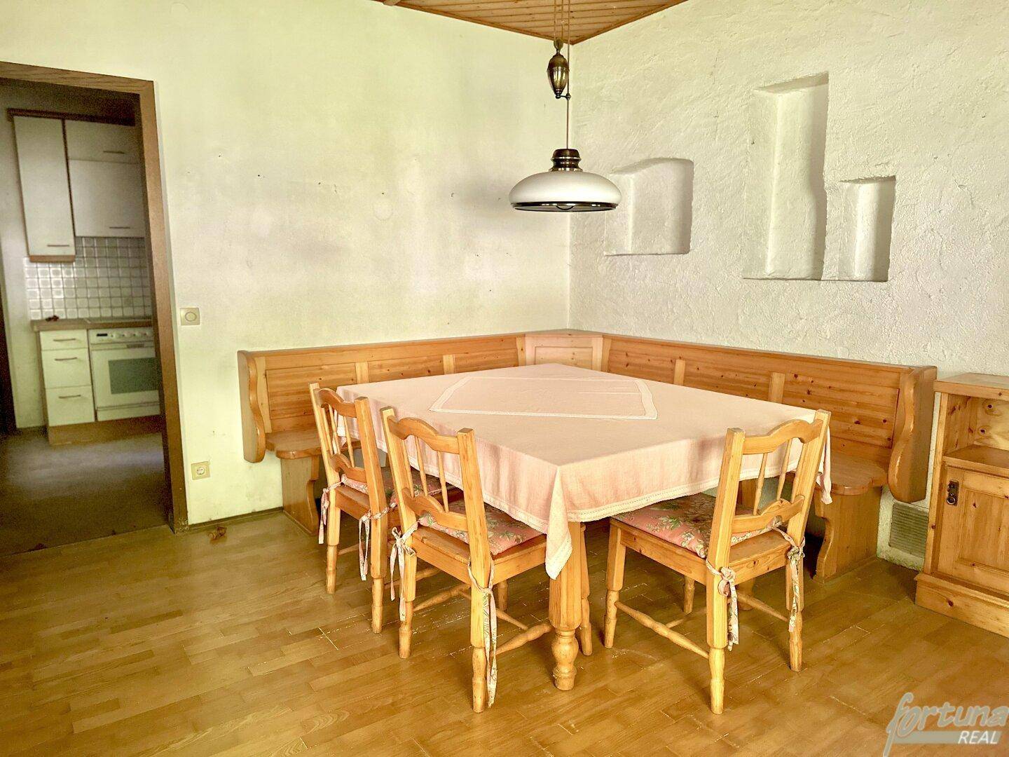 Gemütlicher Essbereich mit Eckbank und Holztisch, angrenzend an eine kleine Küche.