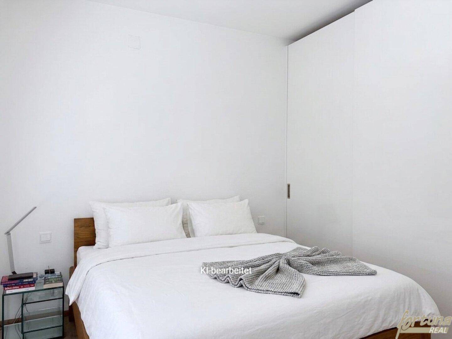 Helles Schlafzimmer mit minimalistischer Einrichtung, weiß gestrichenen Wänden und Holzbett.