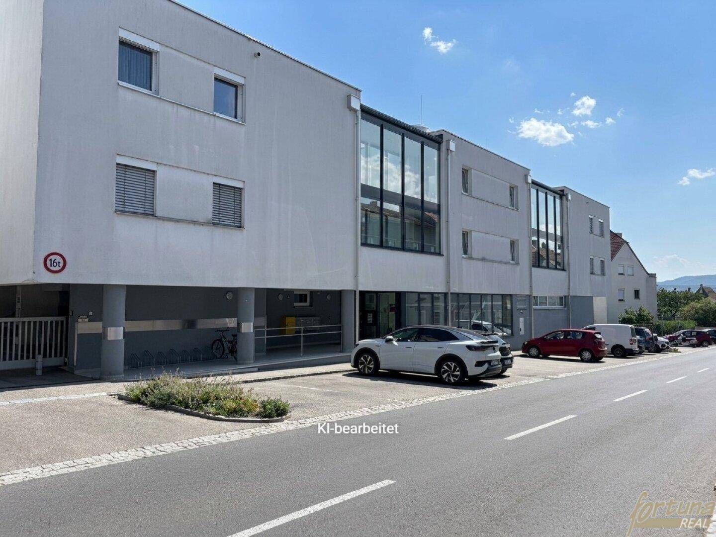 Moderne Gebäudefassade mit großen Glasflächen und Parkplätzen an der Straße.