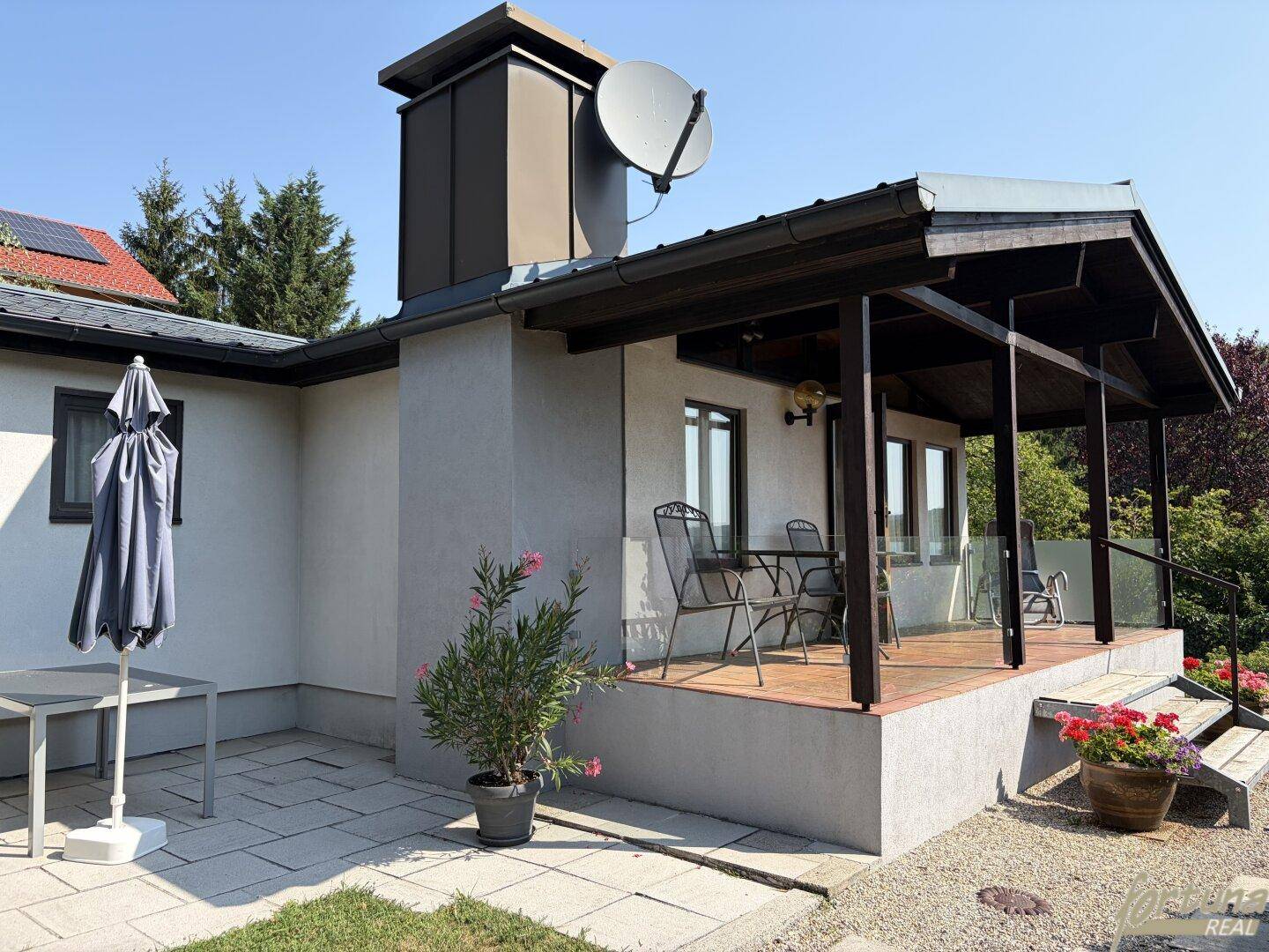 Außenansicht des Hauses mit Terrasse, Gartenmöbeln und Schirm.