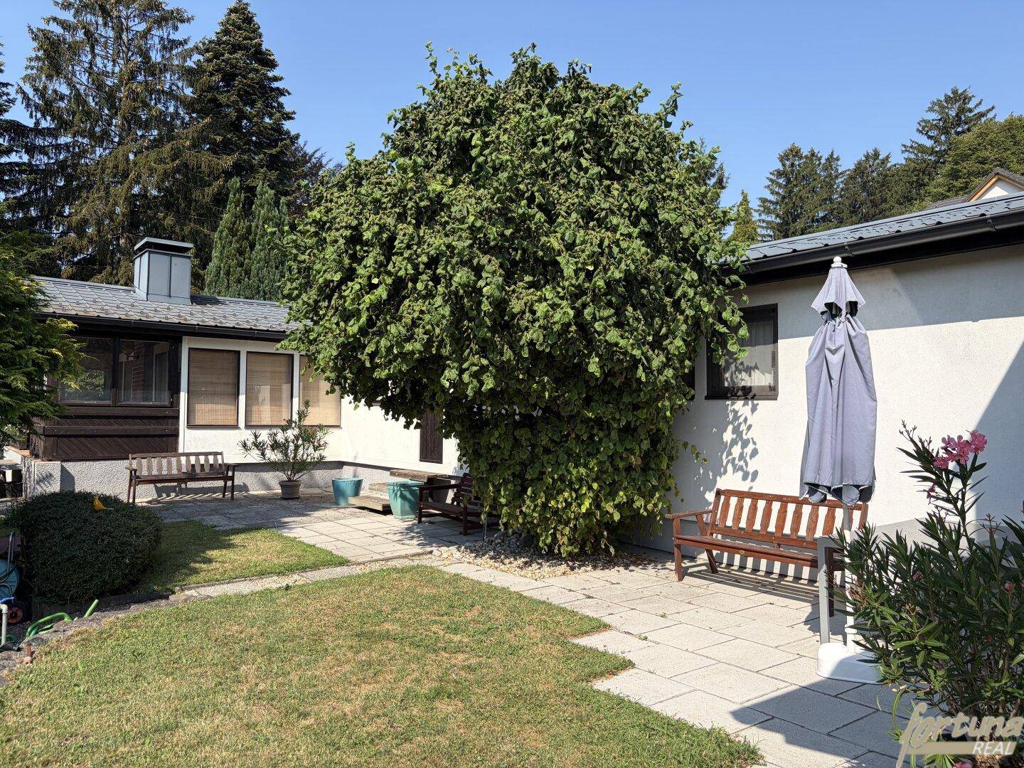 Gepflegter Gartenbereich mit Rasenfläche, gepflasterter Terrasse und Sitzbänken.
