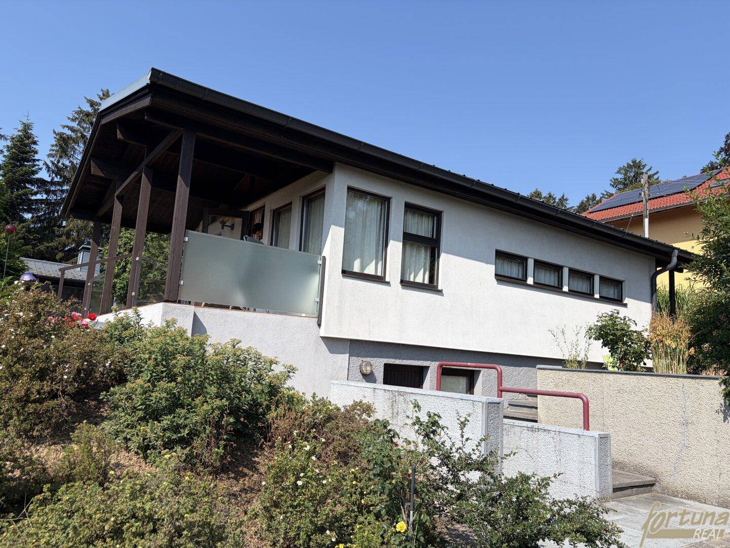 Hausfassade mit überdachter Terrasse und Blick auf die umliegende Natur.