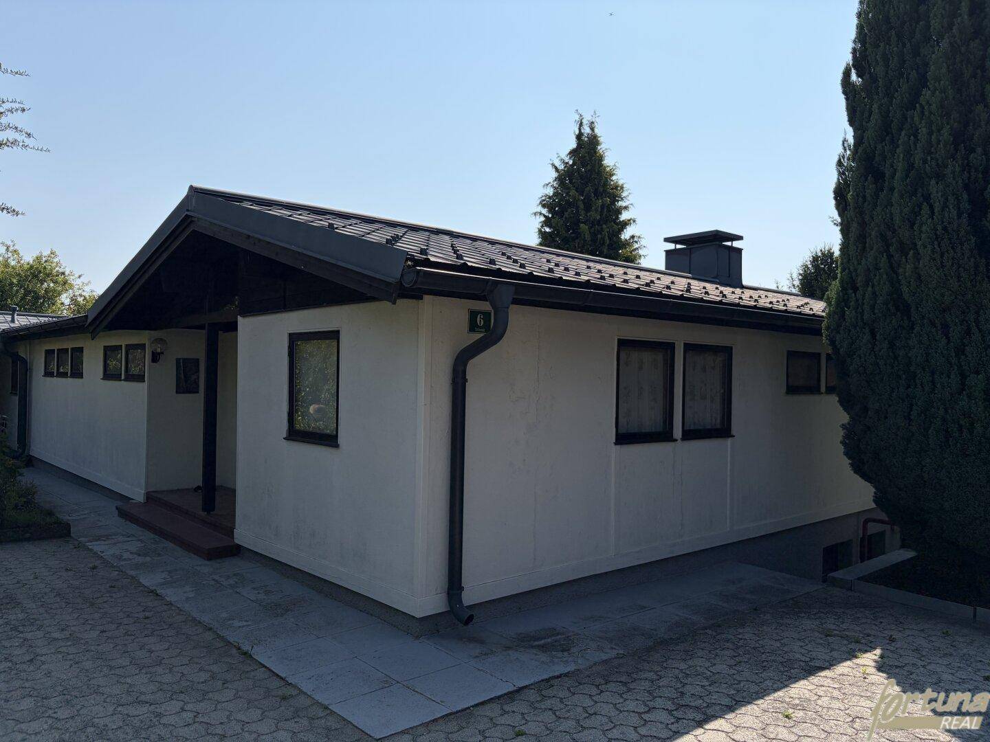 Ansicht des Hauses von der Seite mit gepflastertem Vorplatz und Satteldach.
