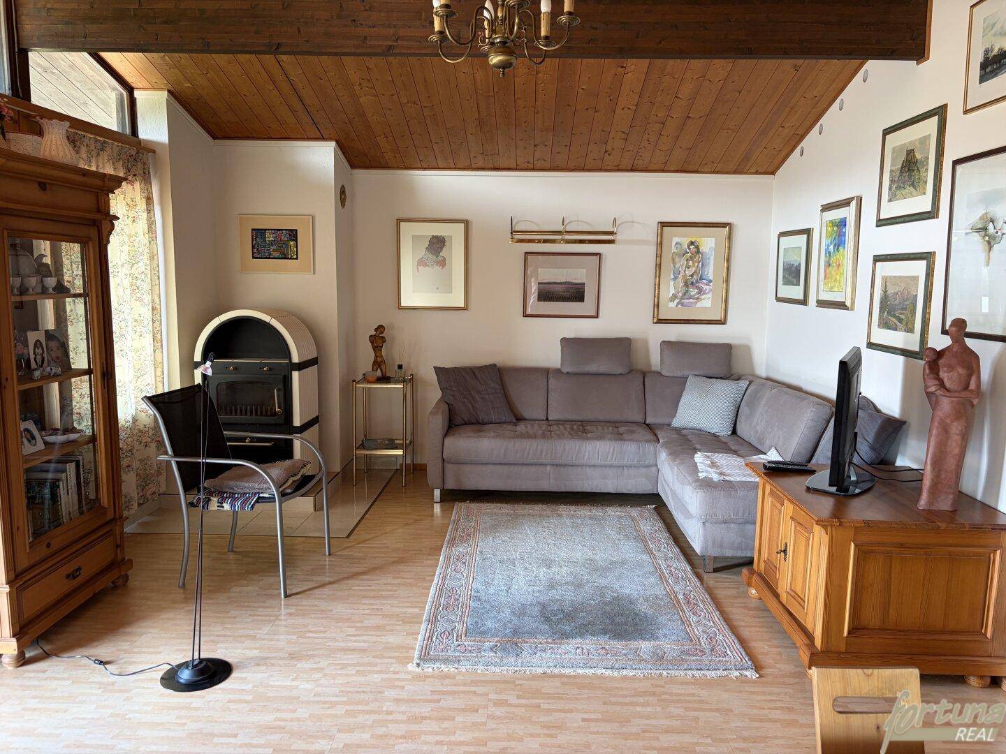 Gemütliches Wohnzimmer mit Ecksofa, Kaminofen und Holzbalkendecke.