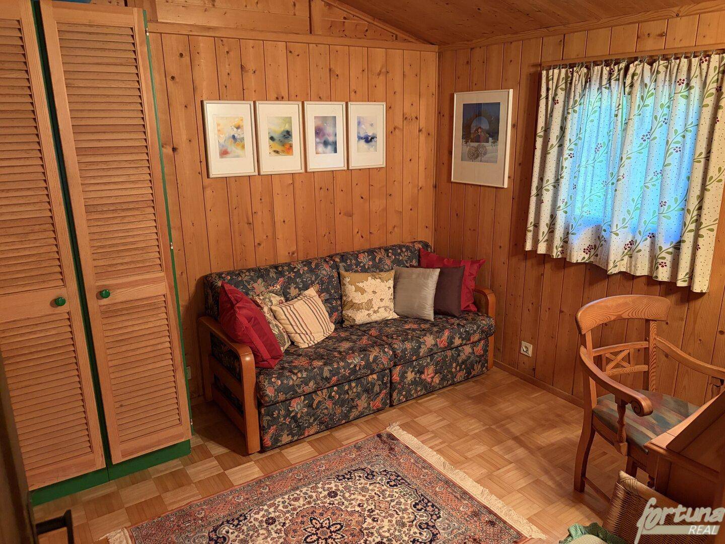 Kleines Schlafzimmer mit Holzvertäfelung, Schlafsofa und traditionellem Teppich.