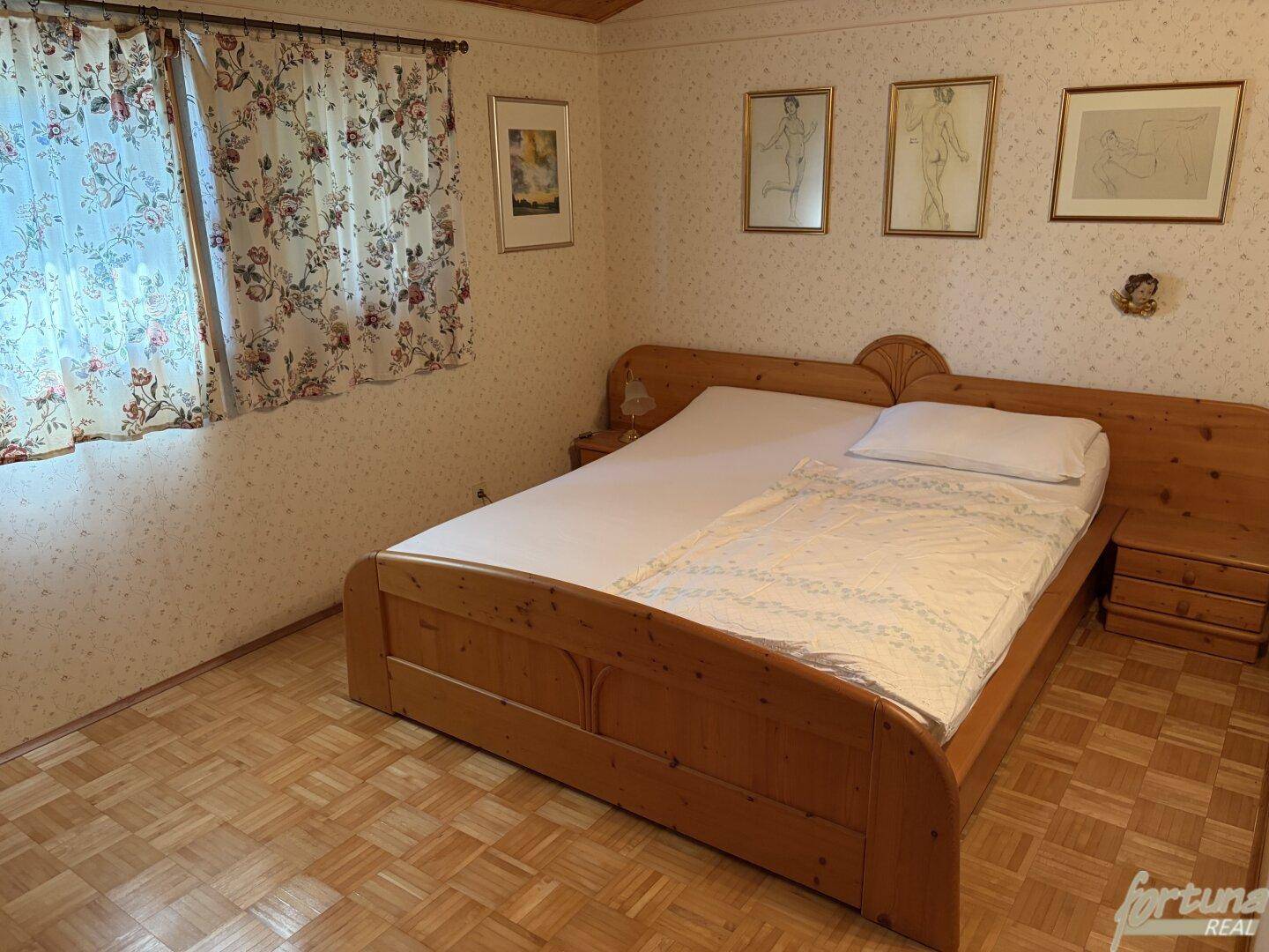 Schlafzimmer mit Doppelbett aus Holz, Nachttischen und gemusterter Tapete.