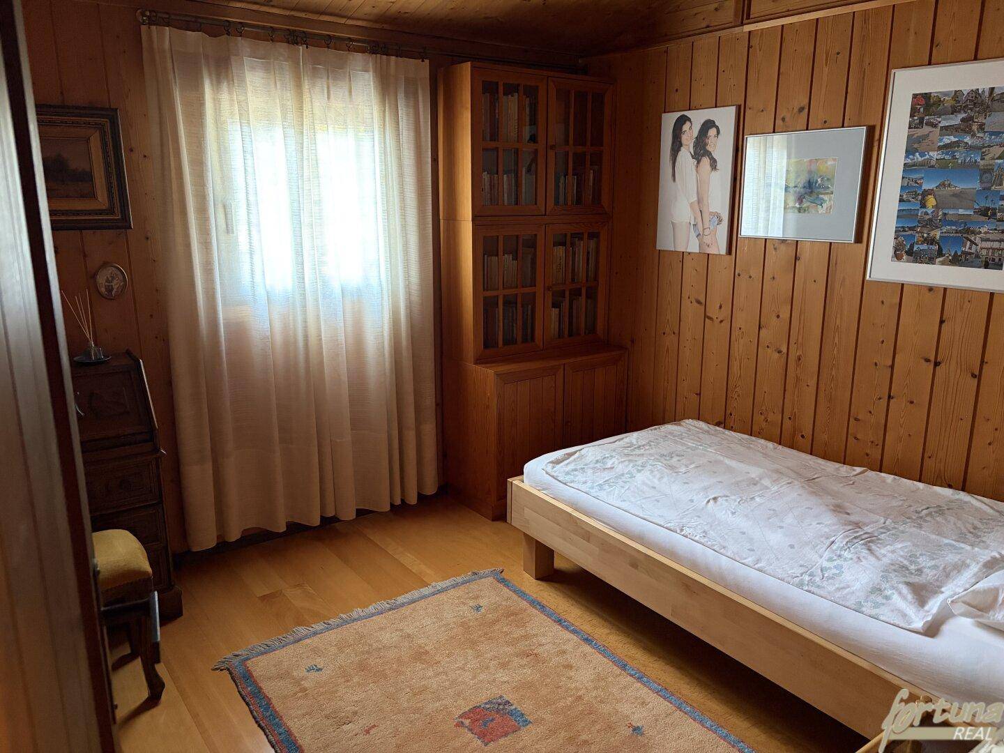 Helles Schlafzimmer mit Einzelbett, Holzvertäfelung und Bücherregal.