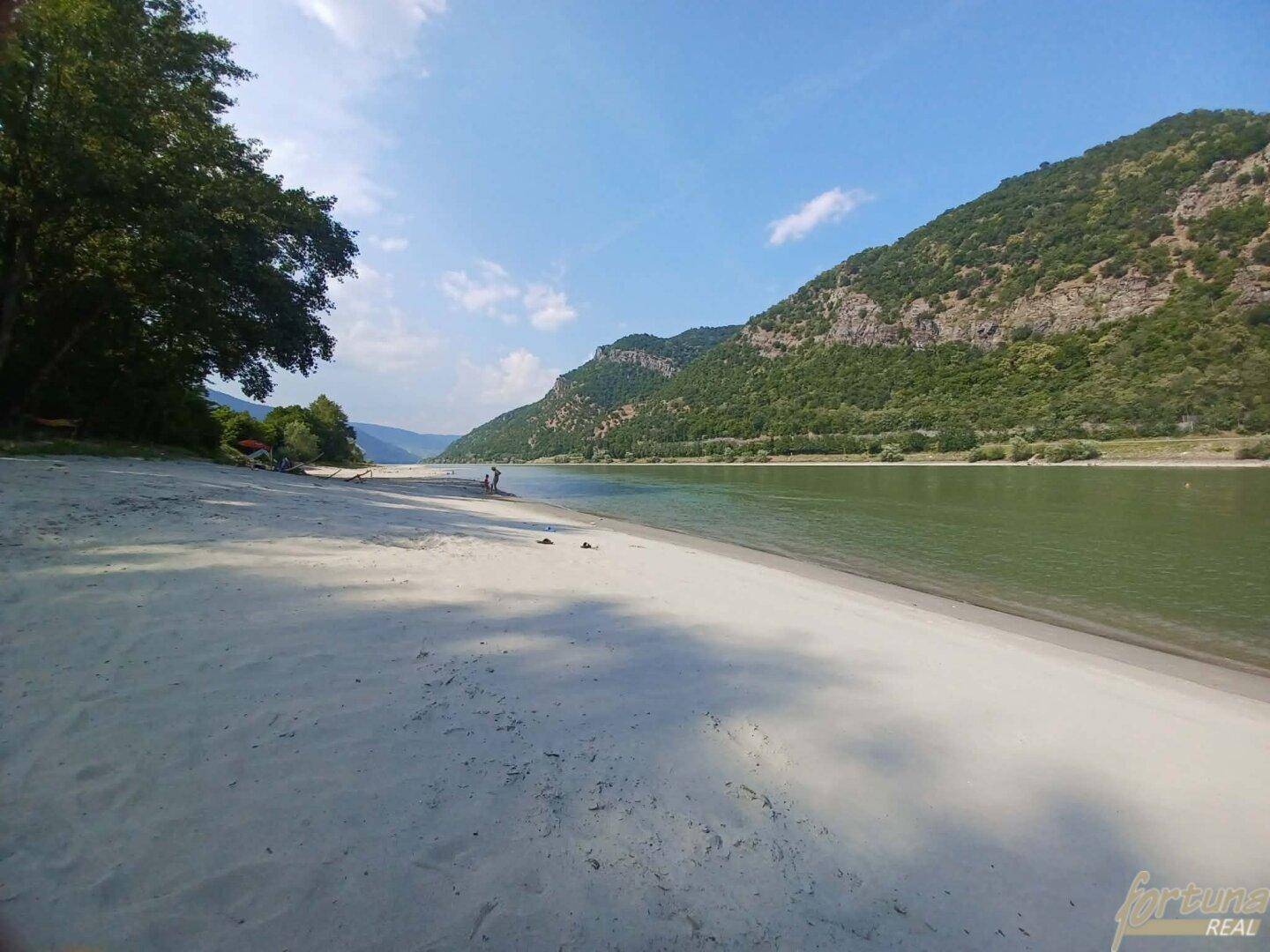 Sandstrand am Flussufer mit majestätischen Bergen im Hintergrund unter strahlend blauem Himmel.