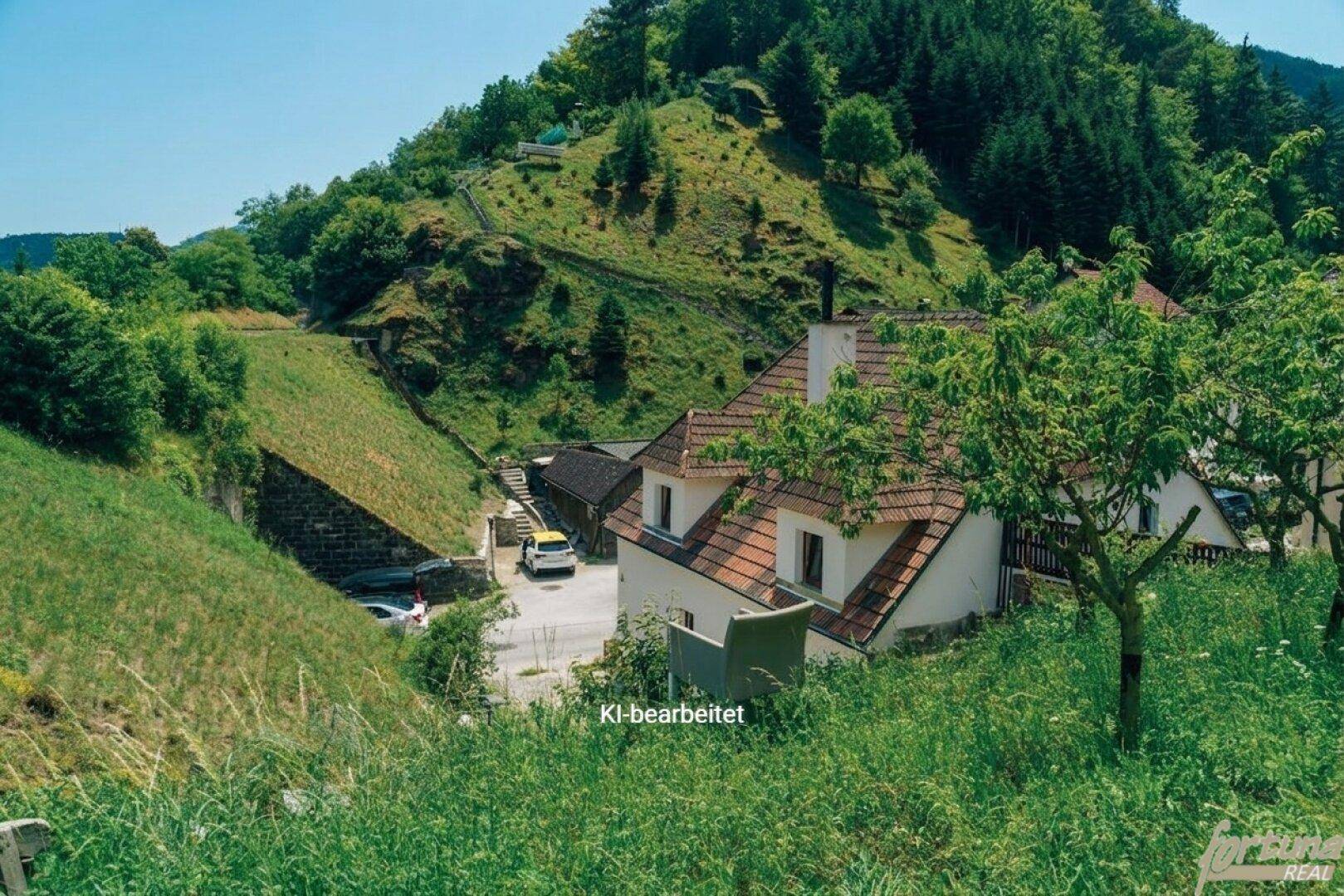 Erhöhte Ansicht des Hauses und der umliegenden Landschaft mit steilen Hängen und Zufahrtsstraße.