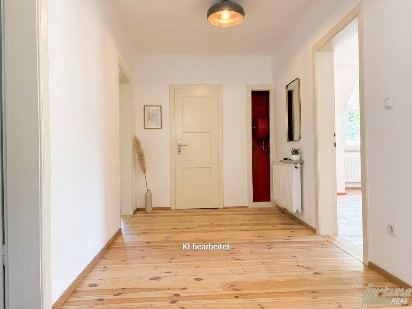 Heller Flur mit Holzdielenboden und weißen Wänden, der zu weiteren Räumen führt.