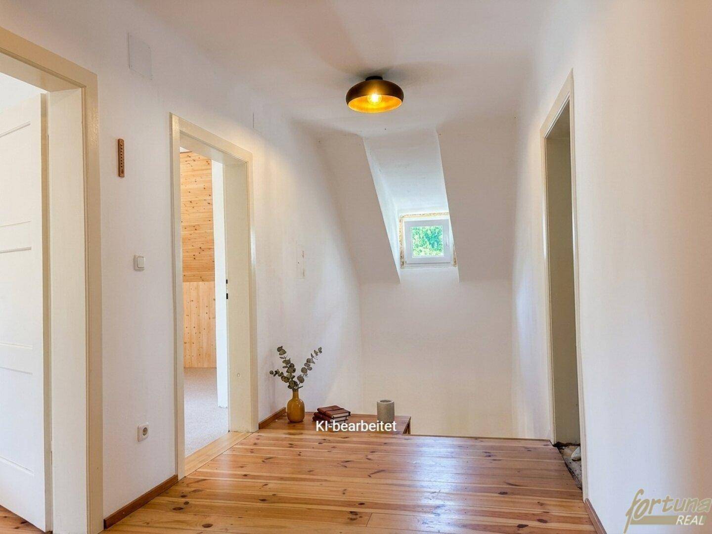 Heller Flur im Obergeschoss mit Holzdielenboden und einem kleinen Fenster am Ende.