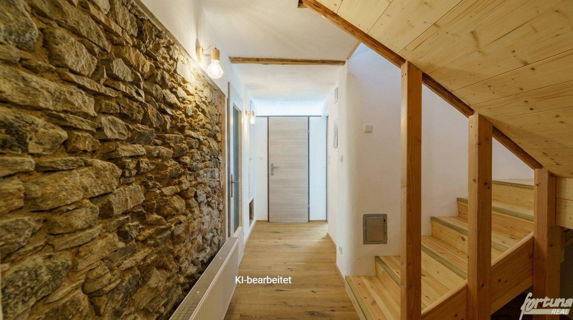Flur mit rustikaler Steinwand und Holztreppe, die in die oberen Stockwerke führt.