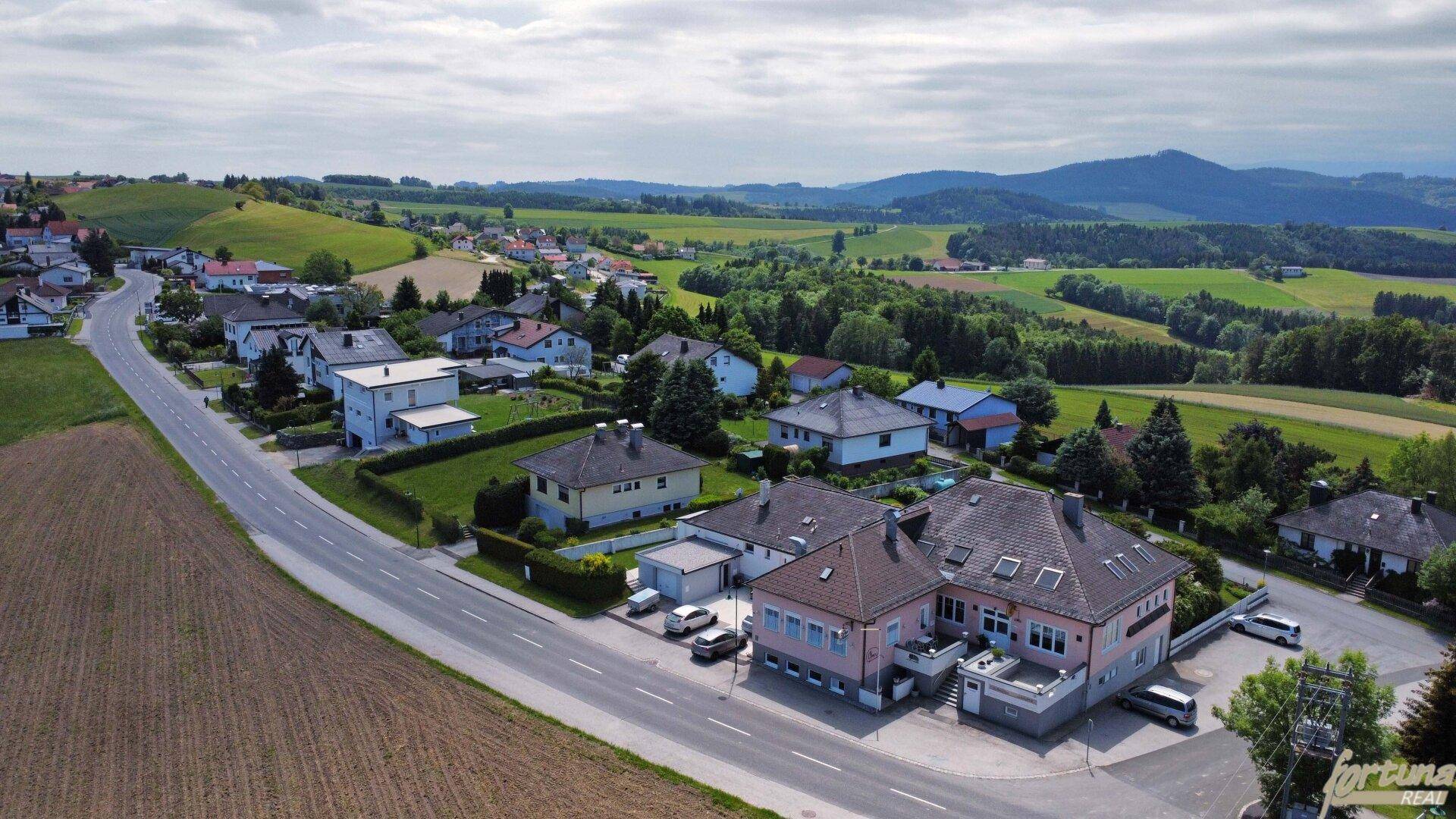 Weitläufige Luftaufnahme des Anwesens in einer grünen, hügeligen Landschaft mit Straße.