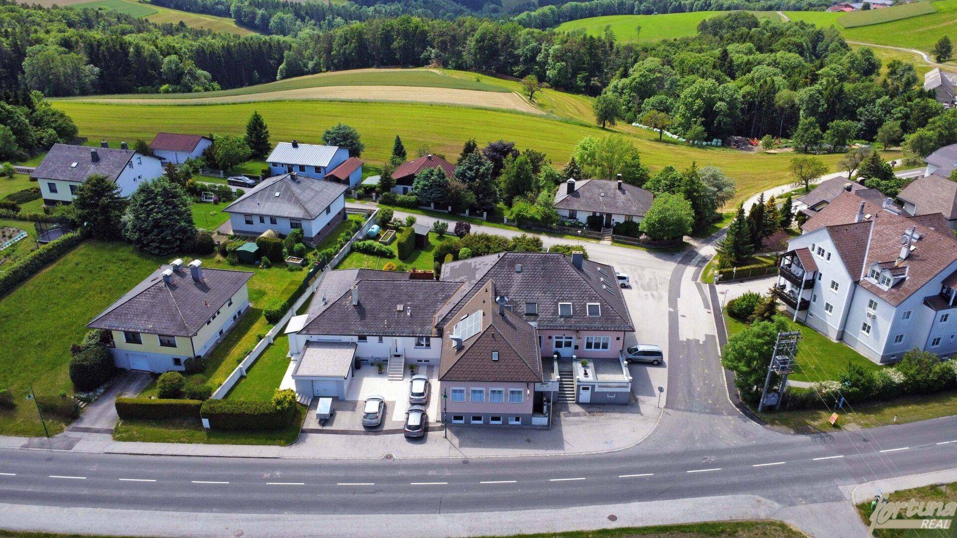 Panoramische Luftaufnahme des Anwesens, umgeben von Feldern und Wäldern unter blauem Himmel.