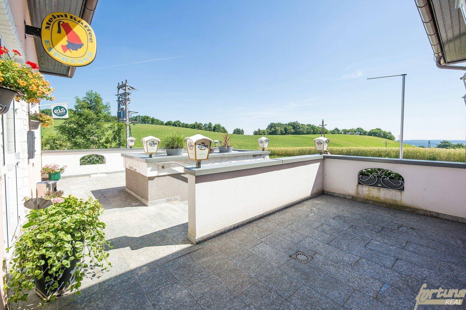Eine geflieste Terrasse mit niedrigen Mauern und weitem Blick auf die grüne Landschaft.