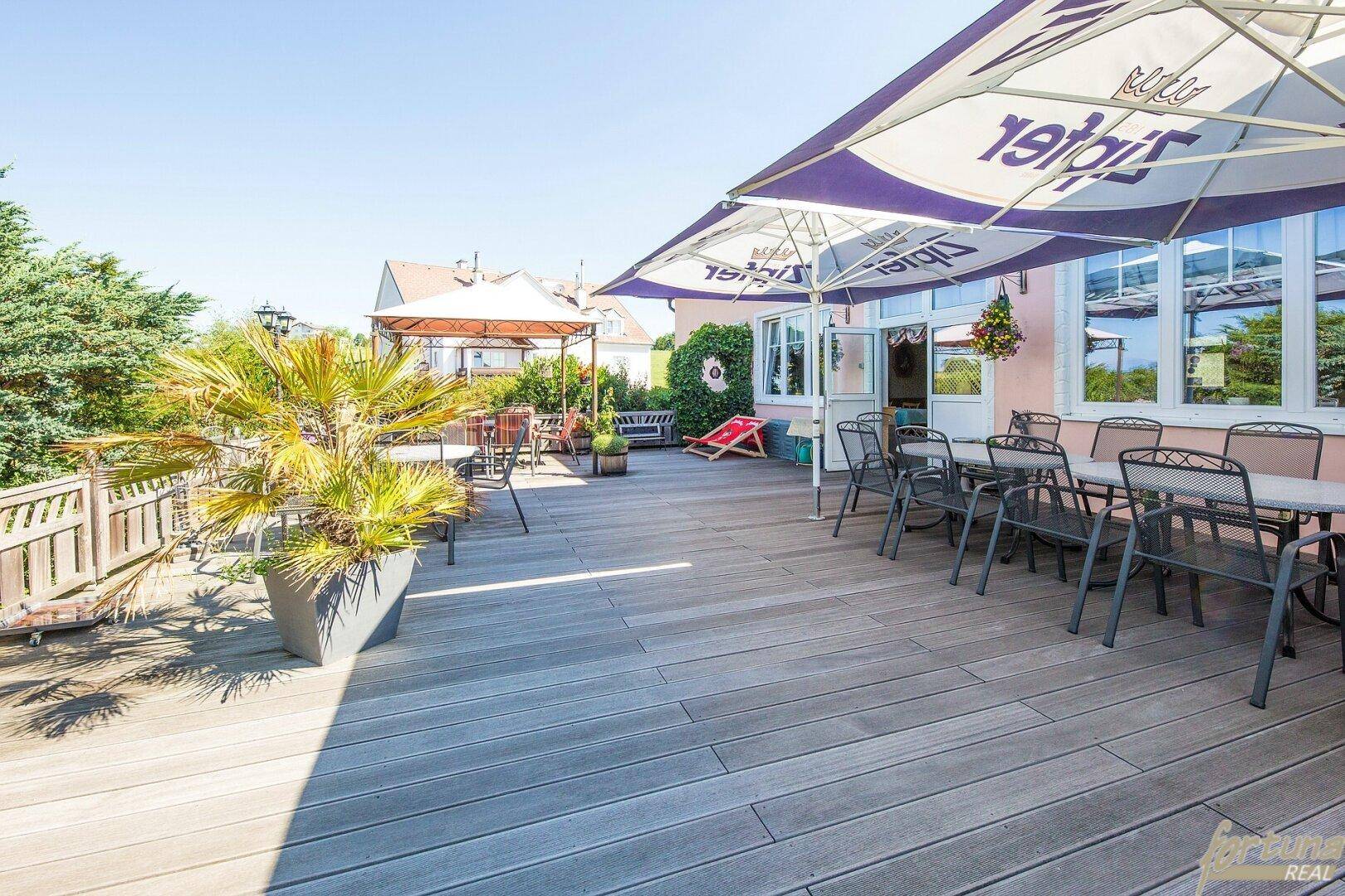 Große Holzterrasse mit Sonnenschirmen, Tischen und Stühlen für den Außenbereich.