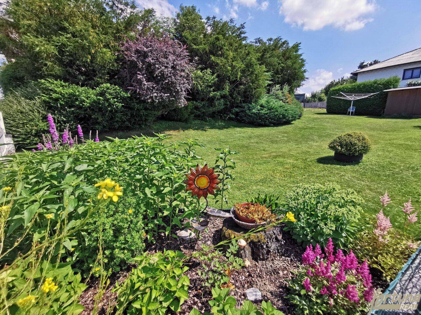 Gepflegter Gartenbereich mit Rasenfläche, Blumenbeeten und üppiger Bepflanzung.