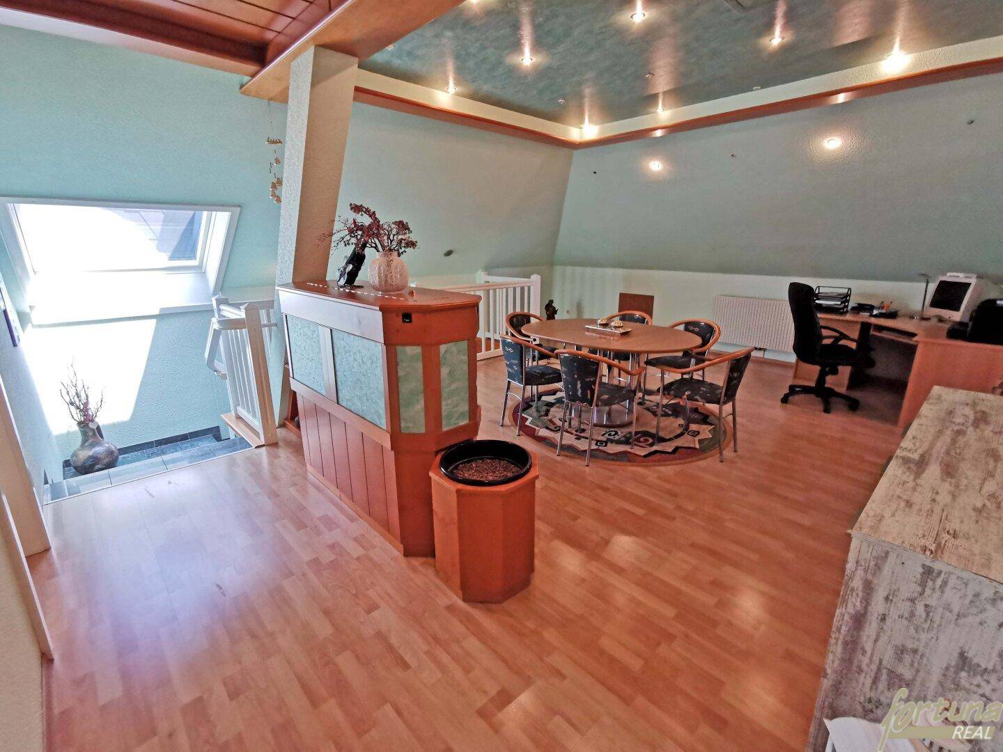 Heller Dachgeschossraum mit Holzboden, Schreibtisch und Sitzbereich unter Dachfenstern.
