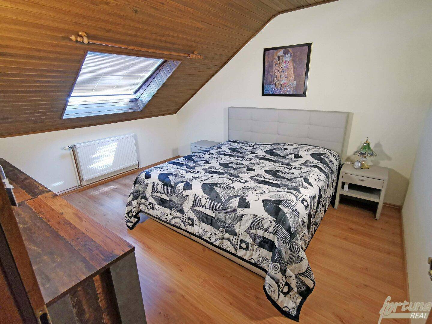 Schlafzimmer im Dachgeschoss mit Holzwänden, Holzboden und Dachfenster.