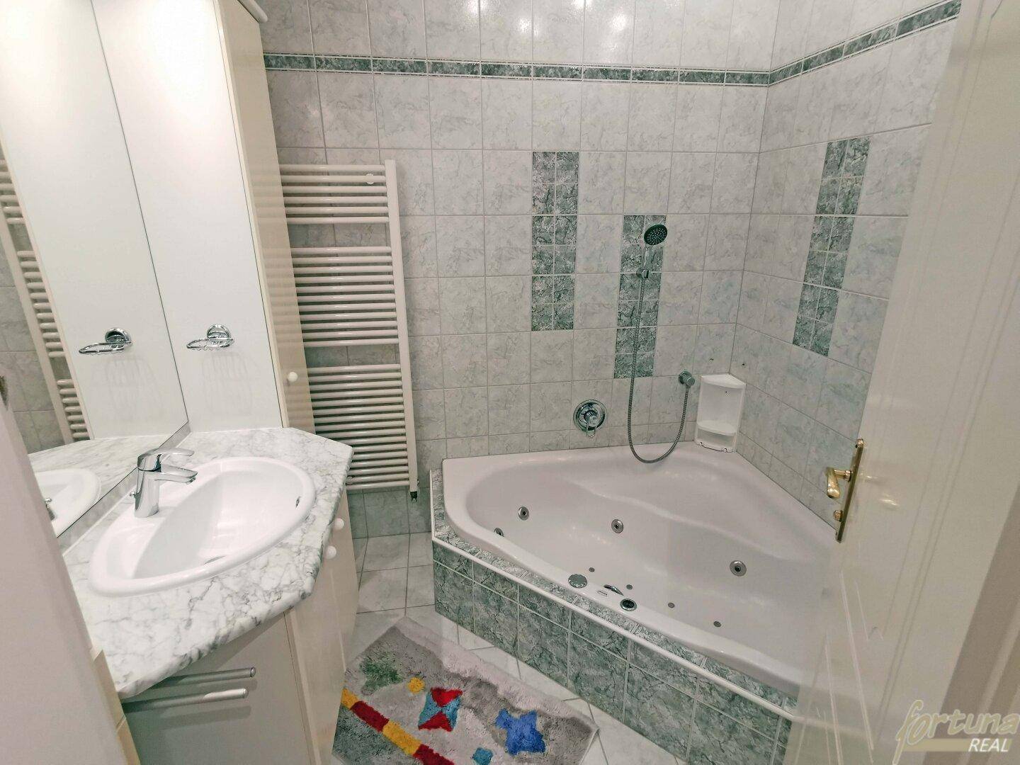 Badezimmer mit Eck-Whirlpool, Einzelwaschbecken und beheiztem Handtuchhalter.
