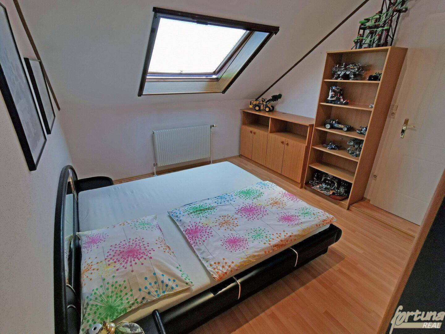 Gemütliches Schlafzimmer im Dachgeschoss mit Holzboden, Dachfenster und Stauraum.