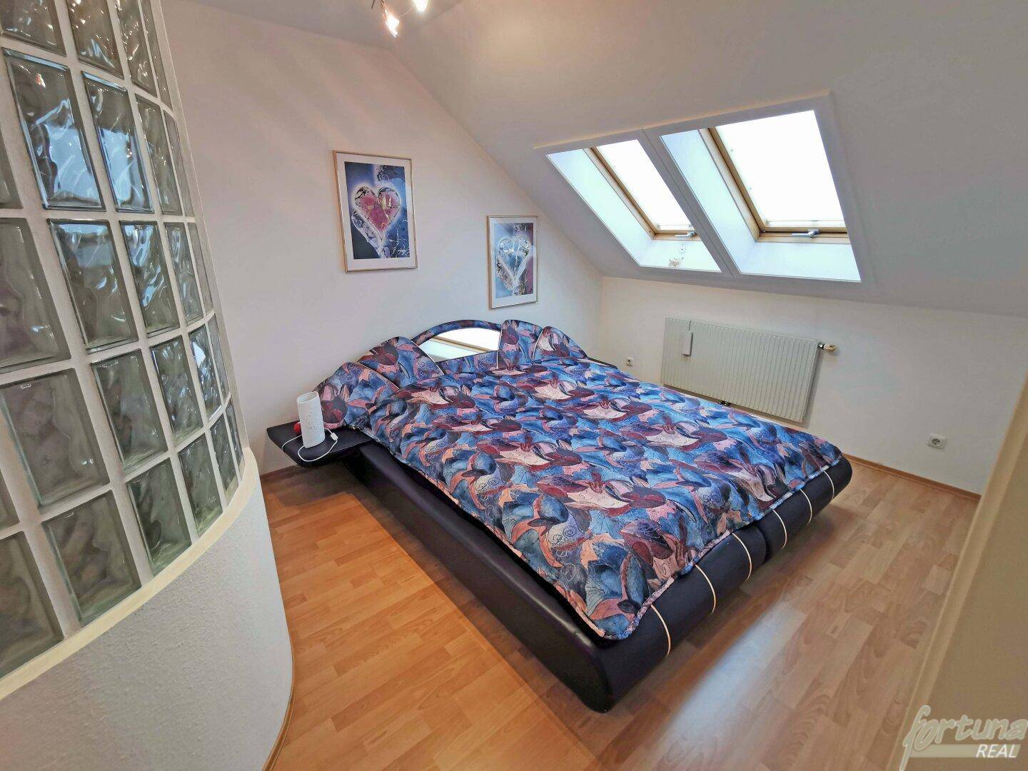 Dachgeschoss-Schlafzimmer mit zwei Dachfenstern, Holzboden und dekorativer Glasbausteinwand.