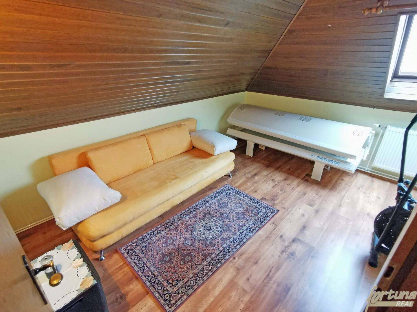Dachgeschossraum mit gelbem Sofa, Teppich und einer Sonnenbank unter Holzverkleidung.