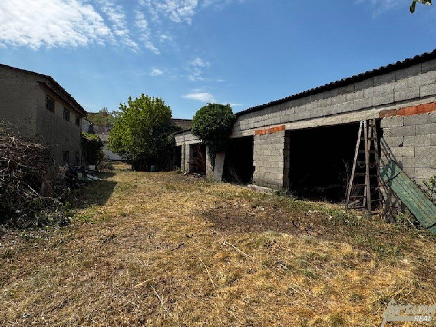 Hinterhofbereich mit mehreren einfachen Nebengebäuden aus Betonblöcken und trockenem Grasboden.