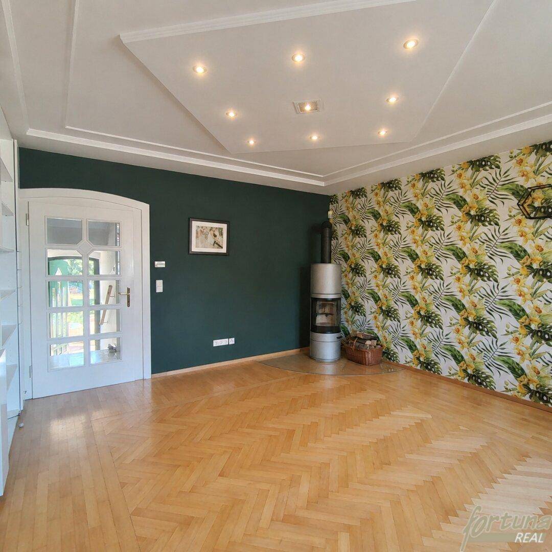 Gemütliches Wohnzimmer mit dunkler Akzentwand, tropischer Tapete und modernem Kaminofen.