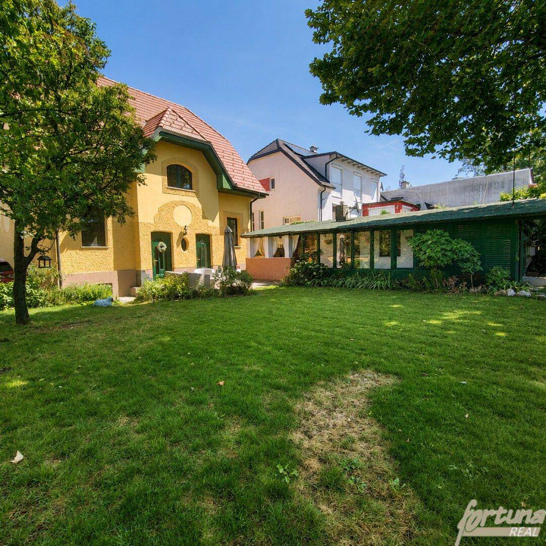 Sonnige Gartenanlage mit gepflegtem Rasen und einem charmanten gelben Haus im Hintergrund.