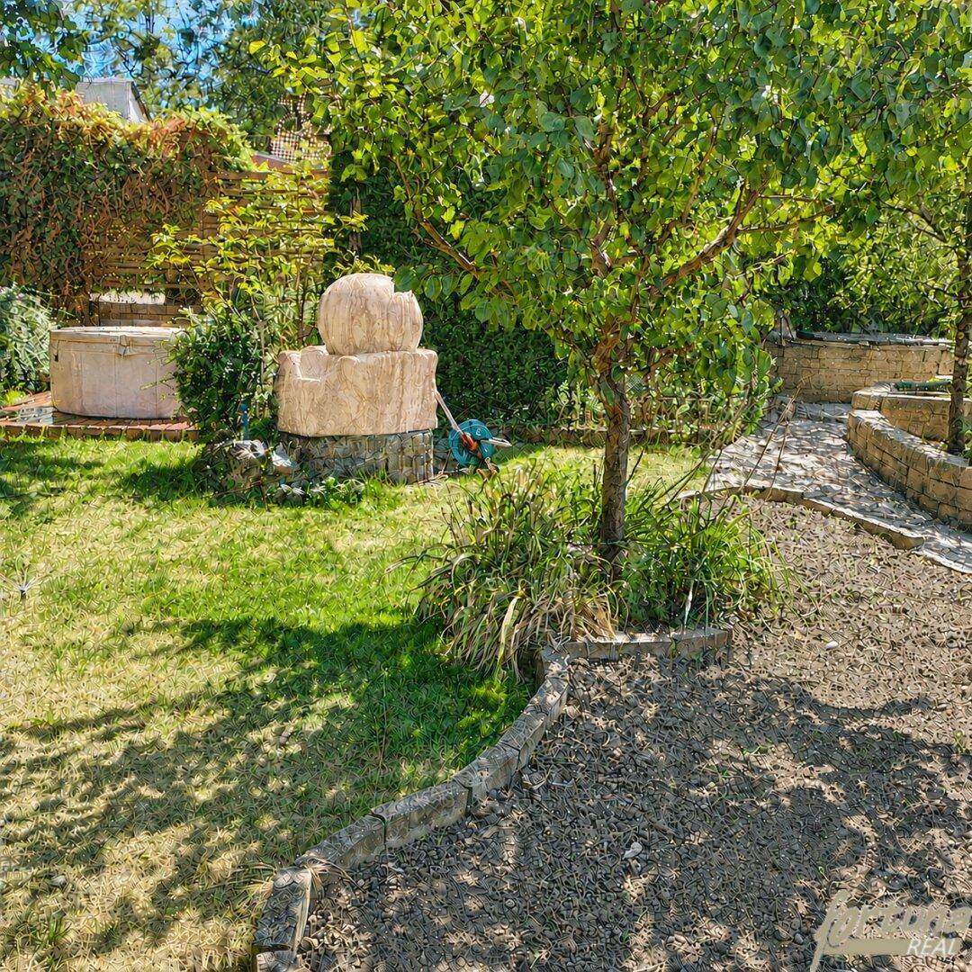 Idyllischer Gartenbereich mit dekorativem Steinbrunnen, jungem Baum und Natursteinbegrenzungen.