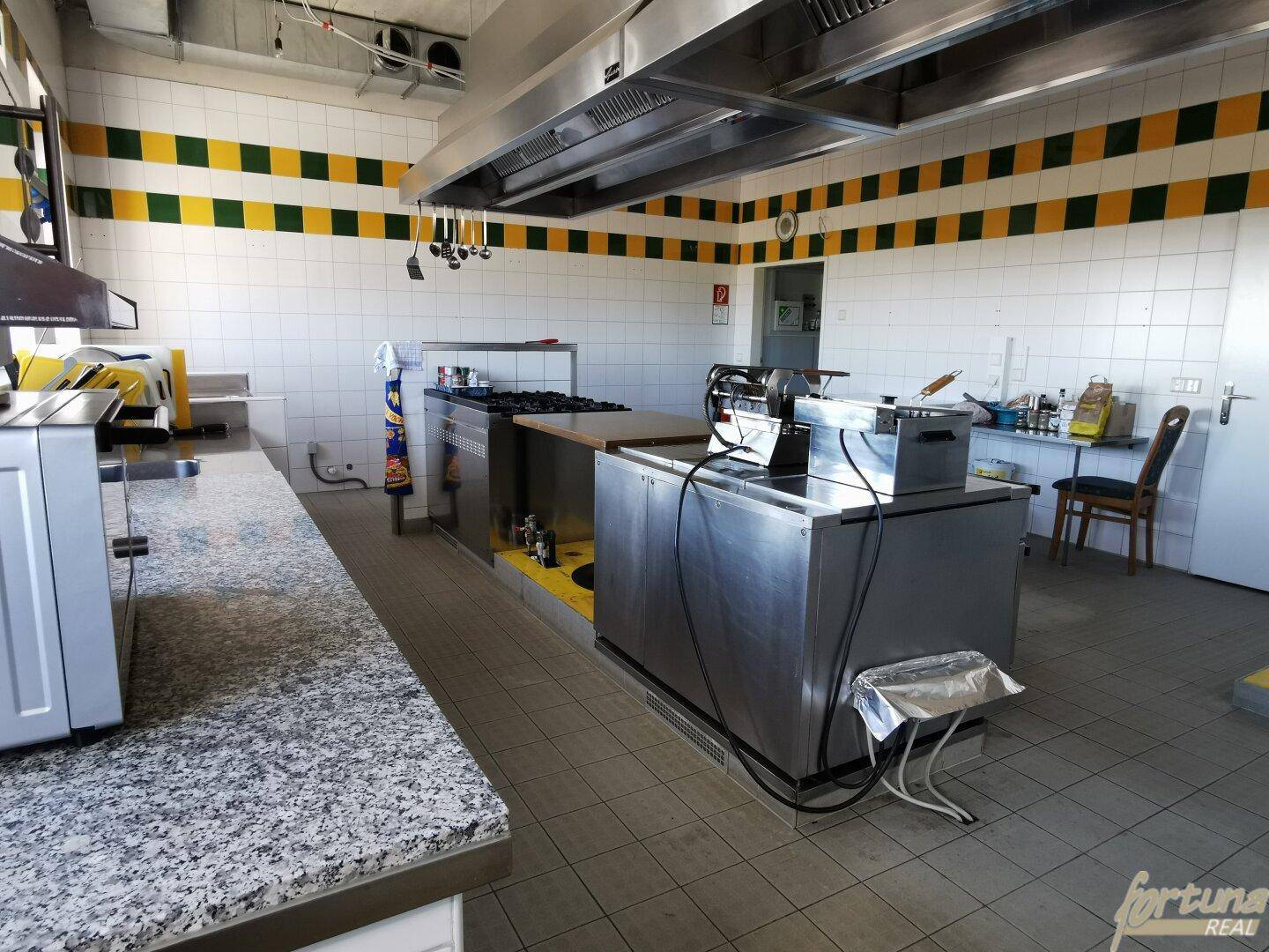 Professionelle Küche mit Edelstahl-Arbeitsflächen, Fliesenboden und großem Abzug.