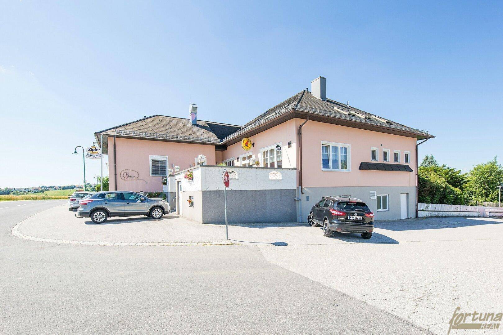 Ansicht des Gebäudes von der Straße mit Parkplätzen und rosa Fassade.